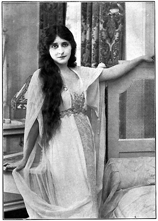 A young woman with long dark hair, standing.